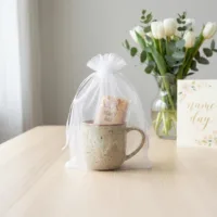 Biały woreczek z organzy 15x20 cm z włożonym do środka ceramicznym kubkiem.