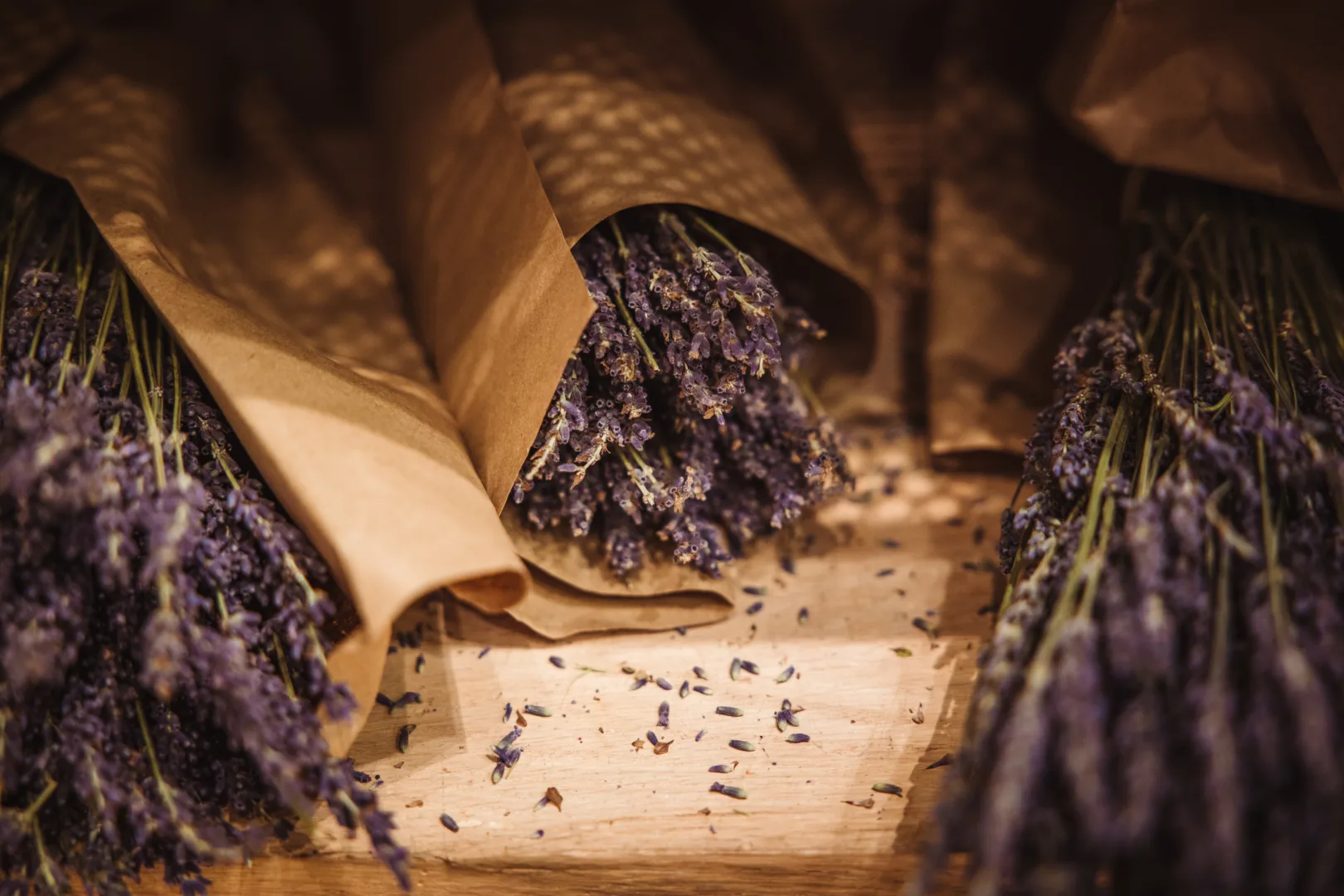 Zbliżenie na bukiety suszonej lawendy w papierowych opakowaniach na drewnianym stole w magazynie plantacji.